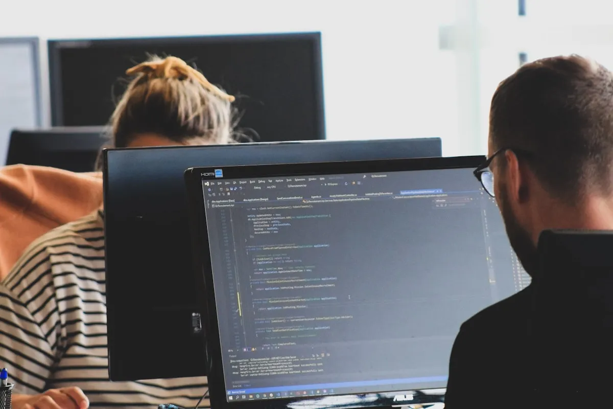 Two engineers reading code on a shared screen in an office, which is where most DevOps consulting time is actually spent